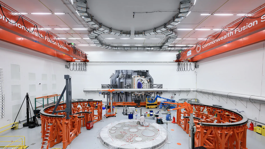Photograph taken at the Commonwealth Fusion Systems headquarters in Devens, Massachusetts. The image shows construction in progress for SPARC, a compact, powerful tokamak machine called SPARC. A rendering of SPARC when completed is shown on the rear wall. Copyright 2025 Commonwealth Fusion Systems (CFS).